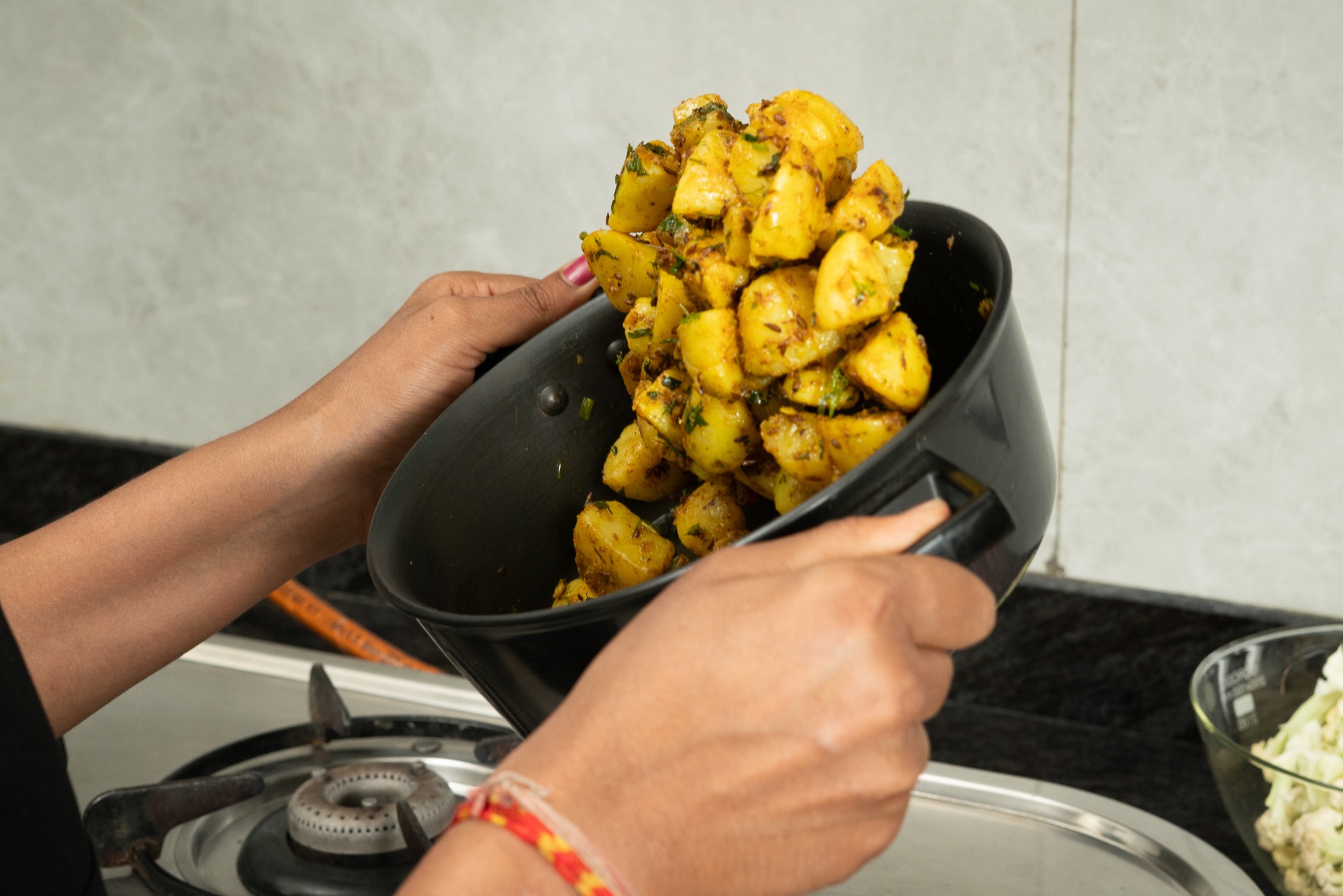 A cook tipping a finished jeera aloo out of the kadhai she cooked it in.